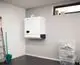 Weißer Wand-Warmwasserspeicher von Vaillant, montiert an einer hellen Wand, mit klaren Linien und einem unteren Fach. Daneben eine Treppe und transparente Aufbewahrungsboxen.